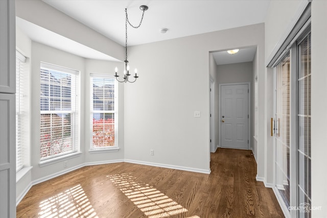 unfurnished dining area featuring plenty of natural light, dark wood-type flooring, and an inviting chandelier