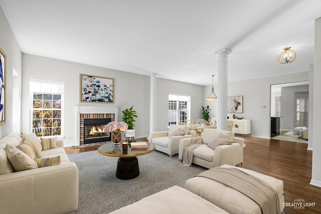 living room featuring dark hardwood / wood-style flooring, decorative columns, and a brick fireplace