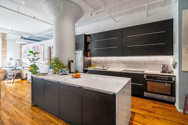 kitchen with oven, sink, light hardwood / wood-style flooring, and tasteful backsplash