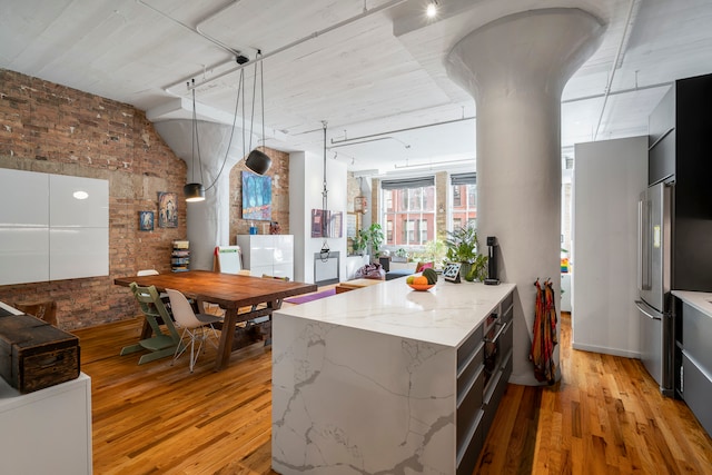 kitchen with light hardwood / wood-style floors, brick wall, light stone countertops, pendant lighting, and high end fridge