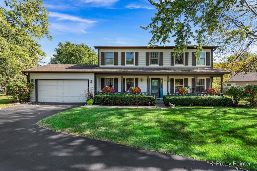 colonial inspired home with a porch, a garage, and a front lawn