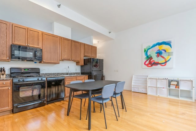 kitchen featuring black appliances, dark stone countertops, sink, and light hardwood / wood-style flooring