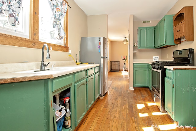 kitchen featuring ceiling fan, sink, stainless steel appliances, green cabinets, and light hardwood / wood-style floors