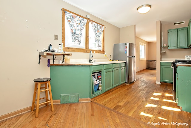 kitchen with stainless steel refrigerator, light wood-type flooring, range with electric stovetop, green cabinetry, and sink