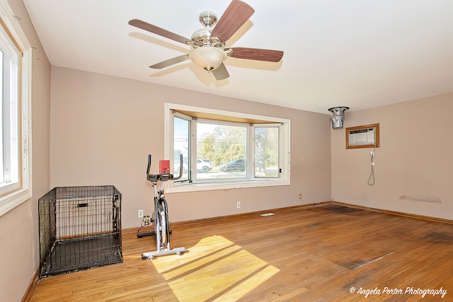 exercise room with light hardwood / wood-style floors, a wall unit AC, and ceiling fan