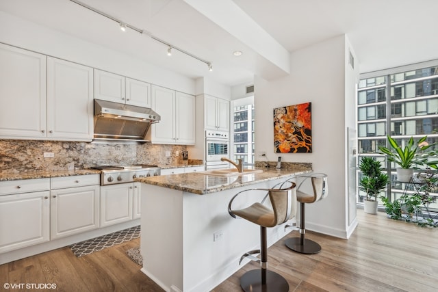 kitchen featuring light stone counters, stainless steel gas stovetop, light hardwood / wood-style floors, and white cabinets