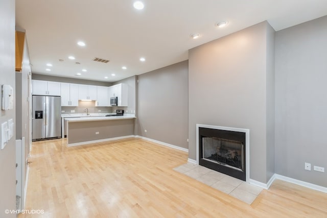 kitchen with appliances with stainless steel finishes, light wood-type flooring, kitchen peninsula, and white cabinetry