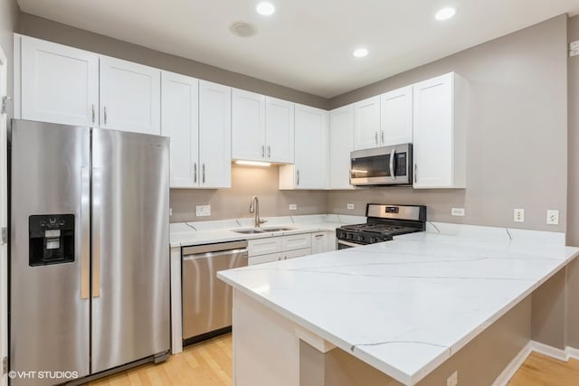 kitchen featuring stainless steel appliances, sink, light hardwood / wood-style floors, kitchen peninsula, and white cabinetry