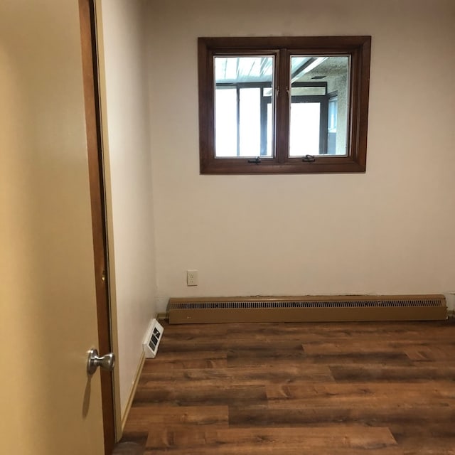 unfurnished room featuring a baseboard heating unit and dark hardwood / wood-style flooring