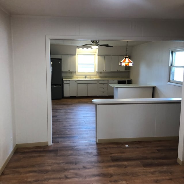 kitchen featuring a healthy amount of sunlight, kitchen peninsula, black fridge, and hanging light fixtures