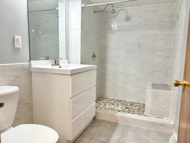 bathroom with a tile shower, vanity, toilet, and tile walls