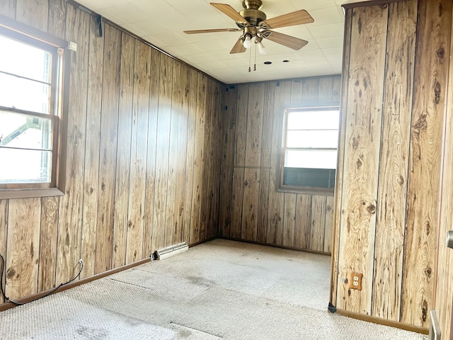 empty room featuring ceiling fan, wood walls, and light carpet