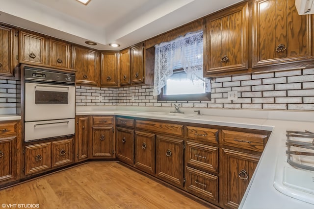 kitchen with tasteful backsplash, oven, light wood-type flooring, and sink