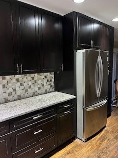 kitchen with stainless steel refrigerator, light stone countertops, light hardwood / wood-style floors, and tasteful backsplash