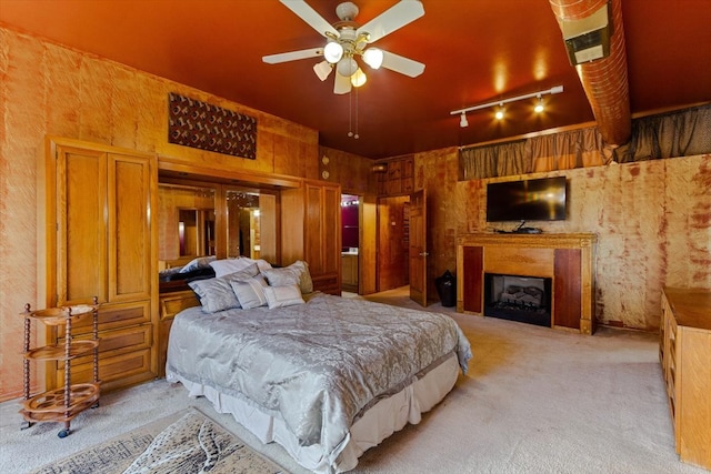 carpeted bedroom featuring rail lighting, wooden walls, and ceiling fan