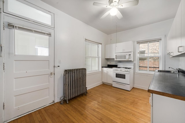 kitchen with sink, white appliances, radiator heating unit, white cabinets, and light wood-type flooring