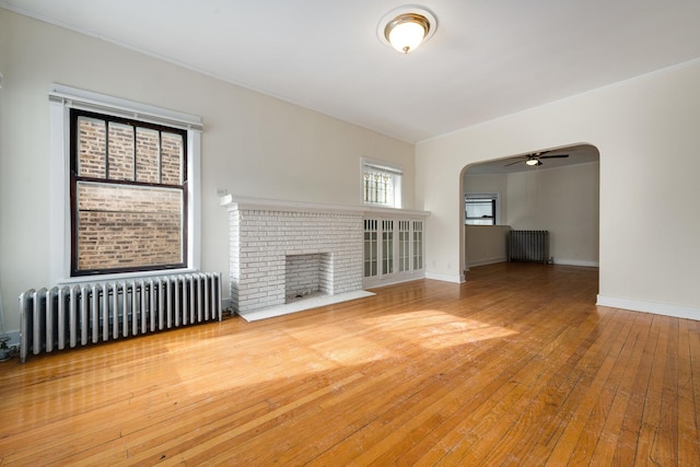 unfurnished living room featuring wood-type flooring, radiator heating unit, ceiling fan, and a fireplace