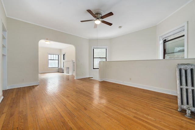 unfurnished living room with ceiling fan, crown molding, radiator heating unit, and light wood-type flooring