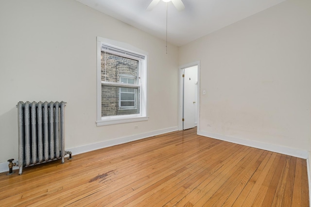 spare room featuring radiator, light wood-style floors, baseboards, and ceiling fan