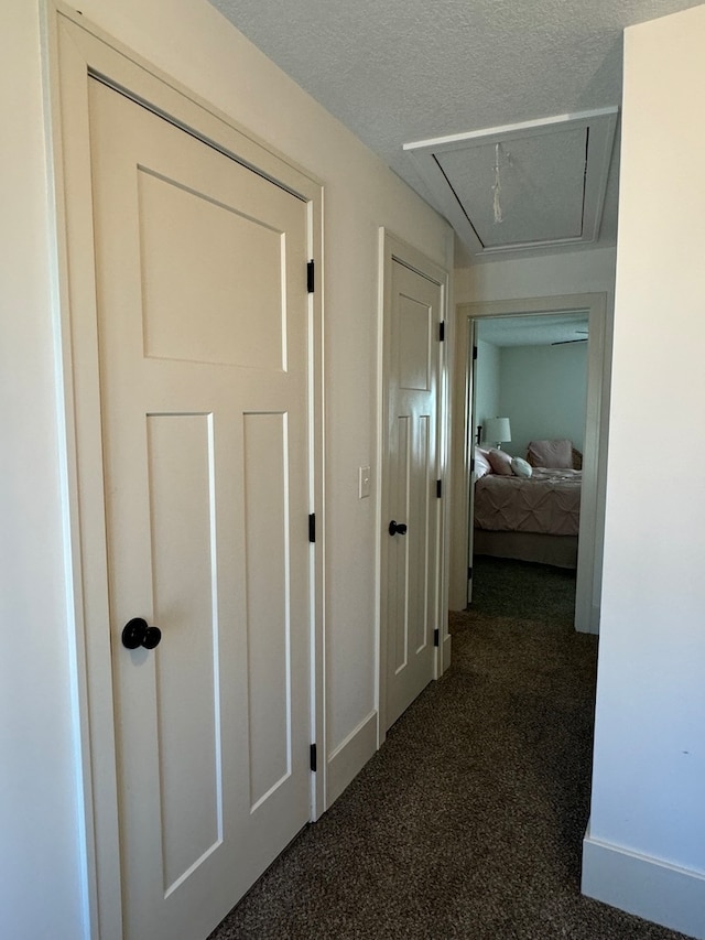 corridor with dark carpet and a textured ceiling