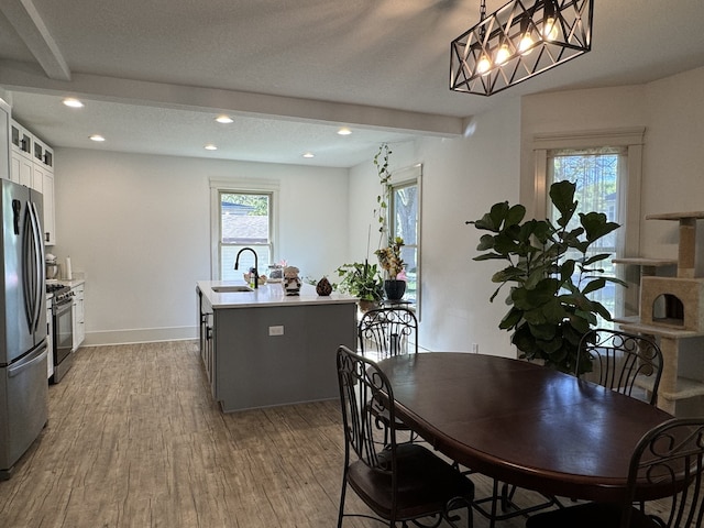 dining area featuring a textured ceiling, light wood-type flooring, beam ceiling, and sink