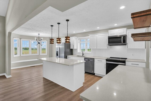 2501 Woodridge Pl, Champaign, IL 61822 - kitchen featuring stainless steel appliances, a kitchen island, a textured ceiling, wood finished floors, and backsplash