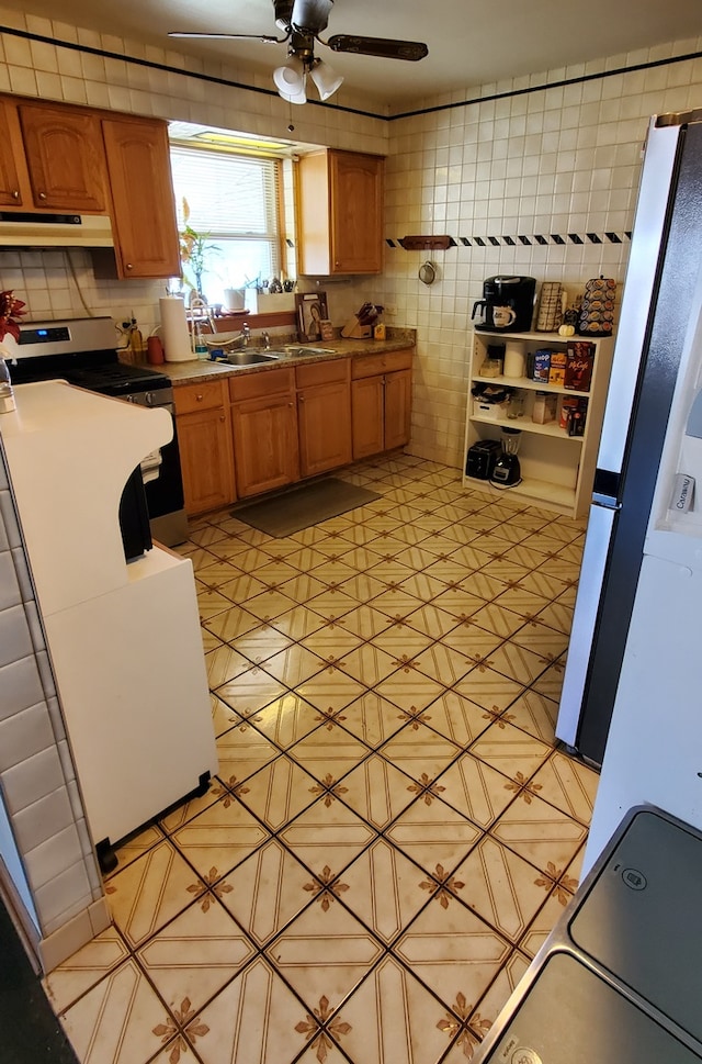 kitchen with ceiling fan, stove, sink, tasteful backsplash, and tile walls