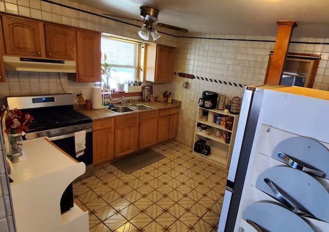 kitchen featuring stainless steel gas range oven, ceiling fan, decorative columns, sink, and white fridge