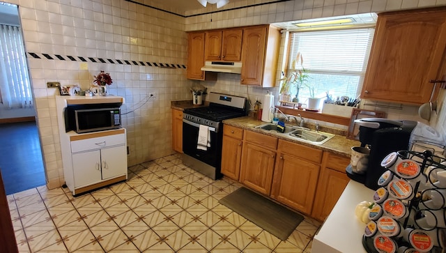 kitchen featuring stainless steel appliances, sink, and tile walls