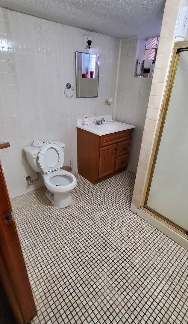 bathroom featuring a textured ceiling, an enclosed shower, vanity, and toilet