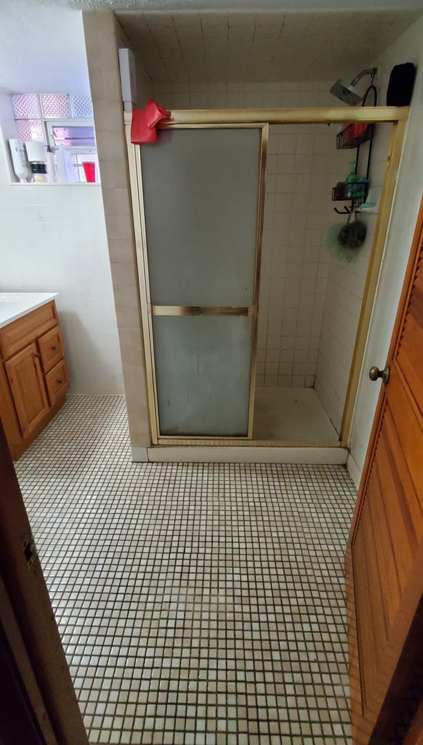 bathroom featuring tile patterned floors, a shower with shower door, and vanity