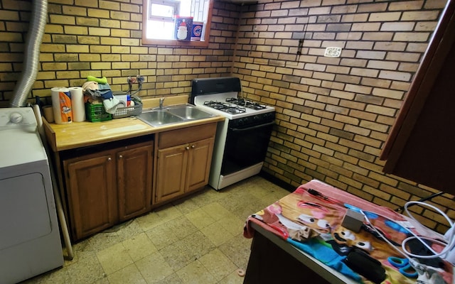 kitchen featuring washer / clothes dryer, brick wall, sink, and white range with gas cooktop