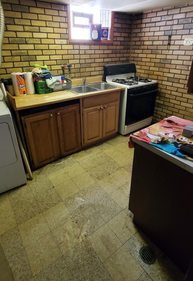 kitchen featuring brick wall, washer / clothes dryer, white range with gas stovetop, and sink