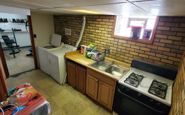 kitchen with washer and clothes dryer, brick wall, sink, and white gas stove