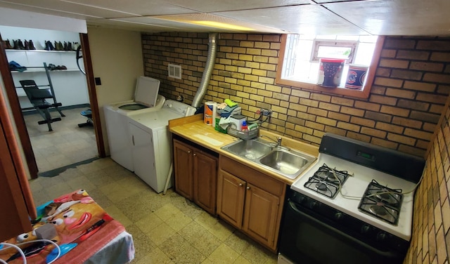 kitchen with sink, brick wall, a paneled ceiling, white gas stove, and washing machine and dryer