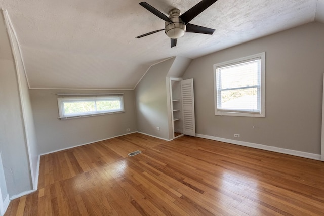 bonus room with lofted ceiling, a wealth of natural light, light hardwood / wood-style floors, and a textured ceiling