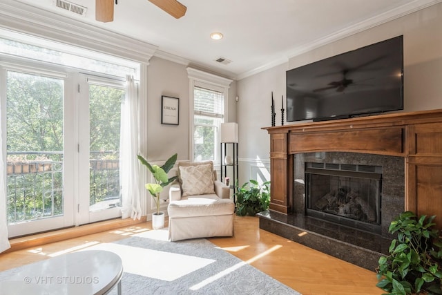 living area with a high end fireplace, ornamental molding, light hardwood / wood-style flooring, and ceiling fan