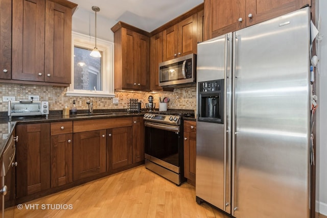 kitchen featuring stainless steel appliances, backsplash, light wood-type flooring, hanging light fixtures, and sink