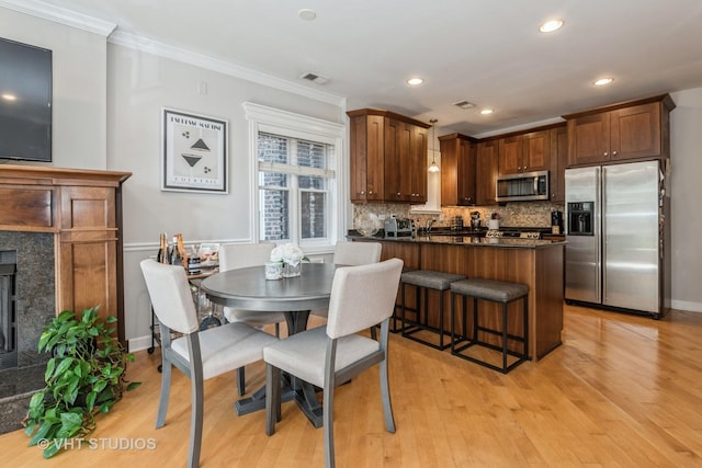 kitchen with light hardwood / wood-style floors, stainless steel appliances, decorative backsplash, ornamental molding, and a high end fireplace