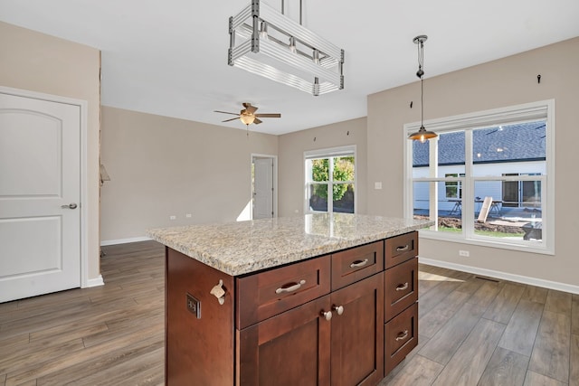 kitchen with light stone counters, ceiling fan, a kitchen island, decorative light fixtures, and light hardwood / wood-style floors