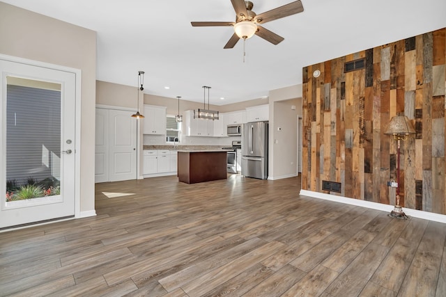 kitchen with pendant lighting, appliances with stainless steel finishes, wood walls, and a kitchen island