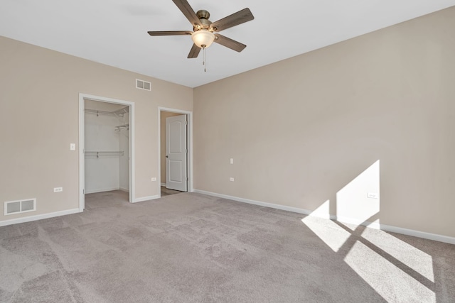 unfurnished bedroom with ceiling fan, light colored carpet, a closet, and a walk in closet