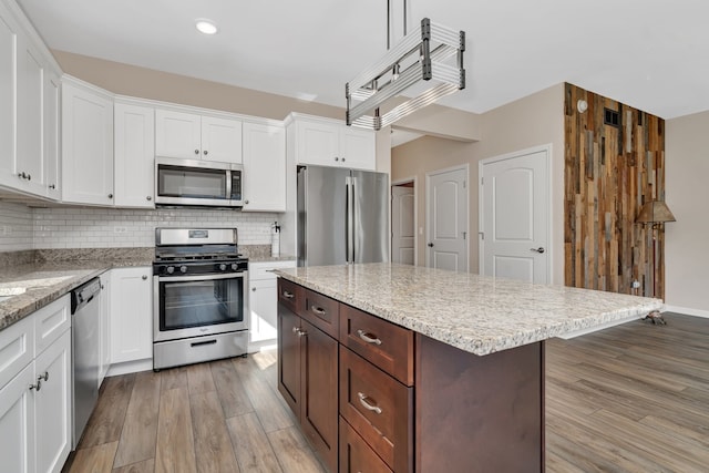 kitchen featuring white cabinets, tasteful backsplash, appliances with stainless steel finishes, a center island, and light hardwood / wood-style floors