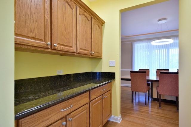 kitchen featuring light wood-type flooring, crown molding, and dark stone counters