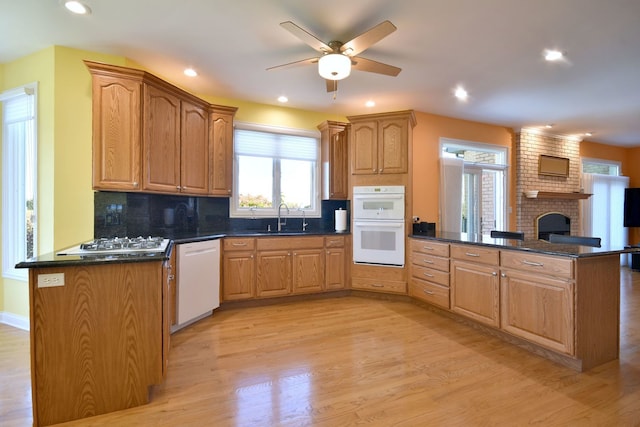 kitchen featuring sink, kitchen peninsula, white appliances, tasteful backsplash, and light wood-type flooring