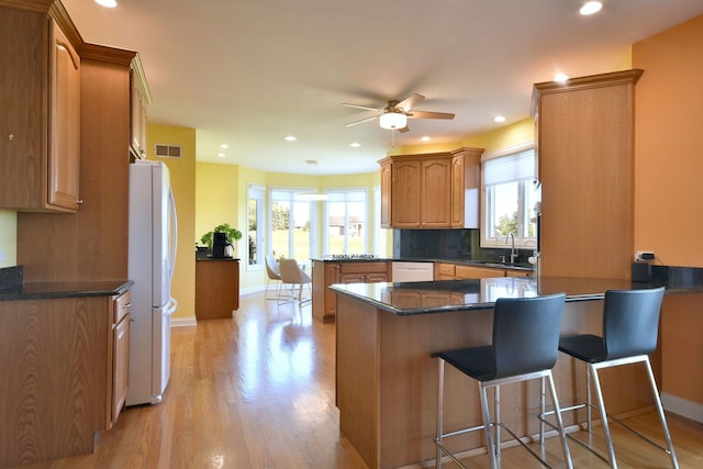 kitchen featuring ceiling fan, white appliances, kitchen peninsula, dark stone counters, and light hardwood / wood-style flooring