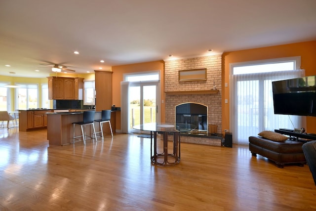 living room featuring a brick fireplace, light wood-type flooring, plenty of natural light, and ceiling fan