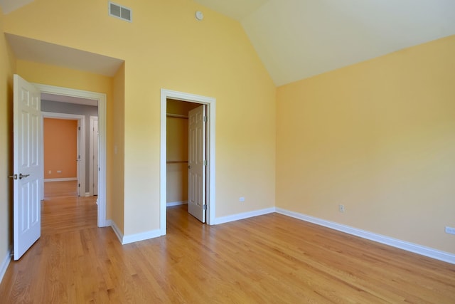 unfurnished bedroom with light wood-type flooring, high vaulted ceiling, a closet, and a walk in closet