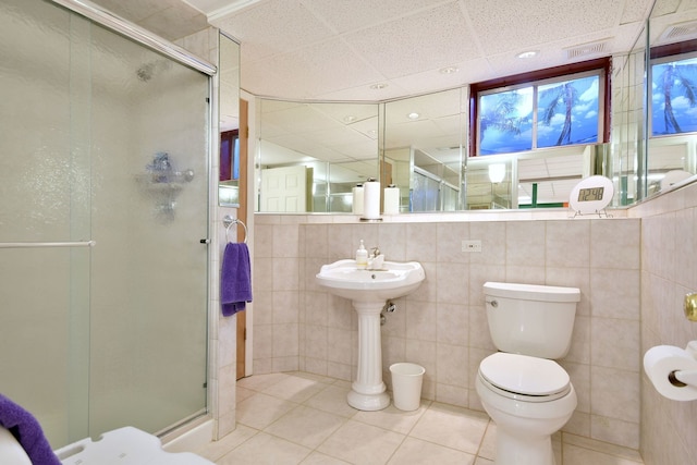 bathroom with an enclosed shower, a drop ceiling, tile patterned floors, tile walls, and toilet