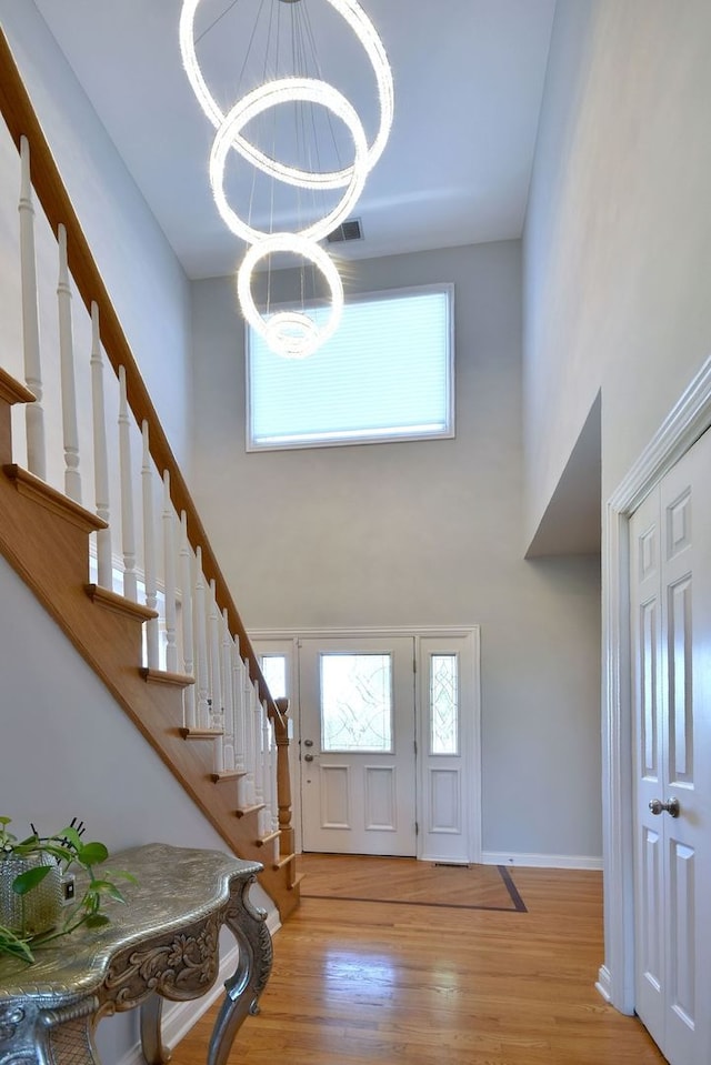 entrance foyer with light wood-type flooring, a towering ceiling, and an inviting chandelier